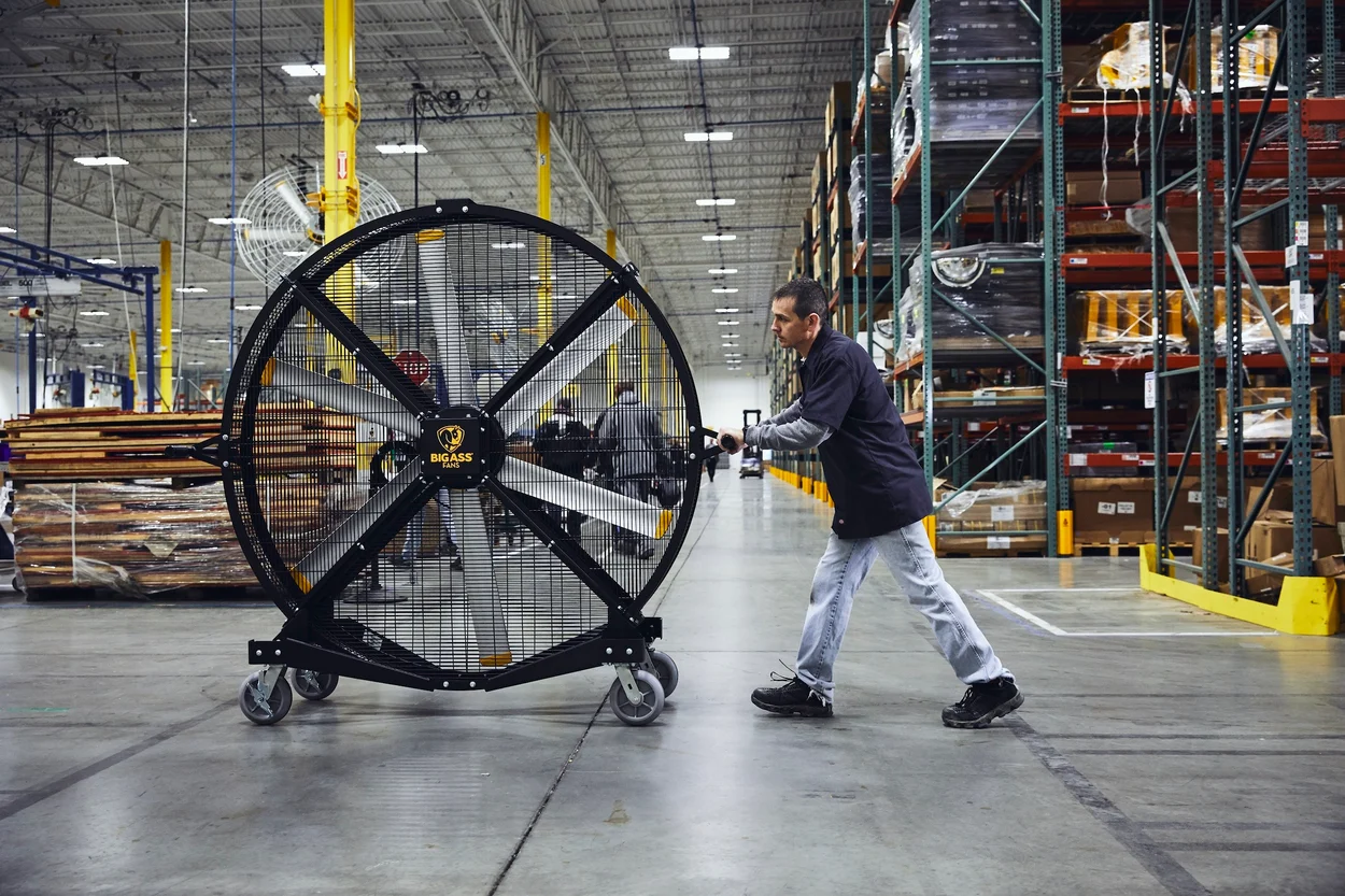 Worker pushing a large Big Ass Fan in an industrial warehouse for ventilation