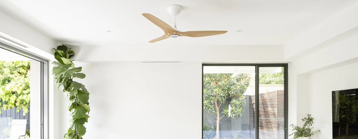 Modern ceiling fan in a bright, minimalistic living room with large windows and greenery outside