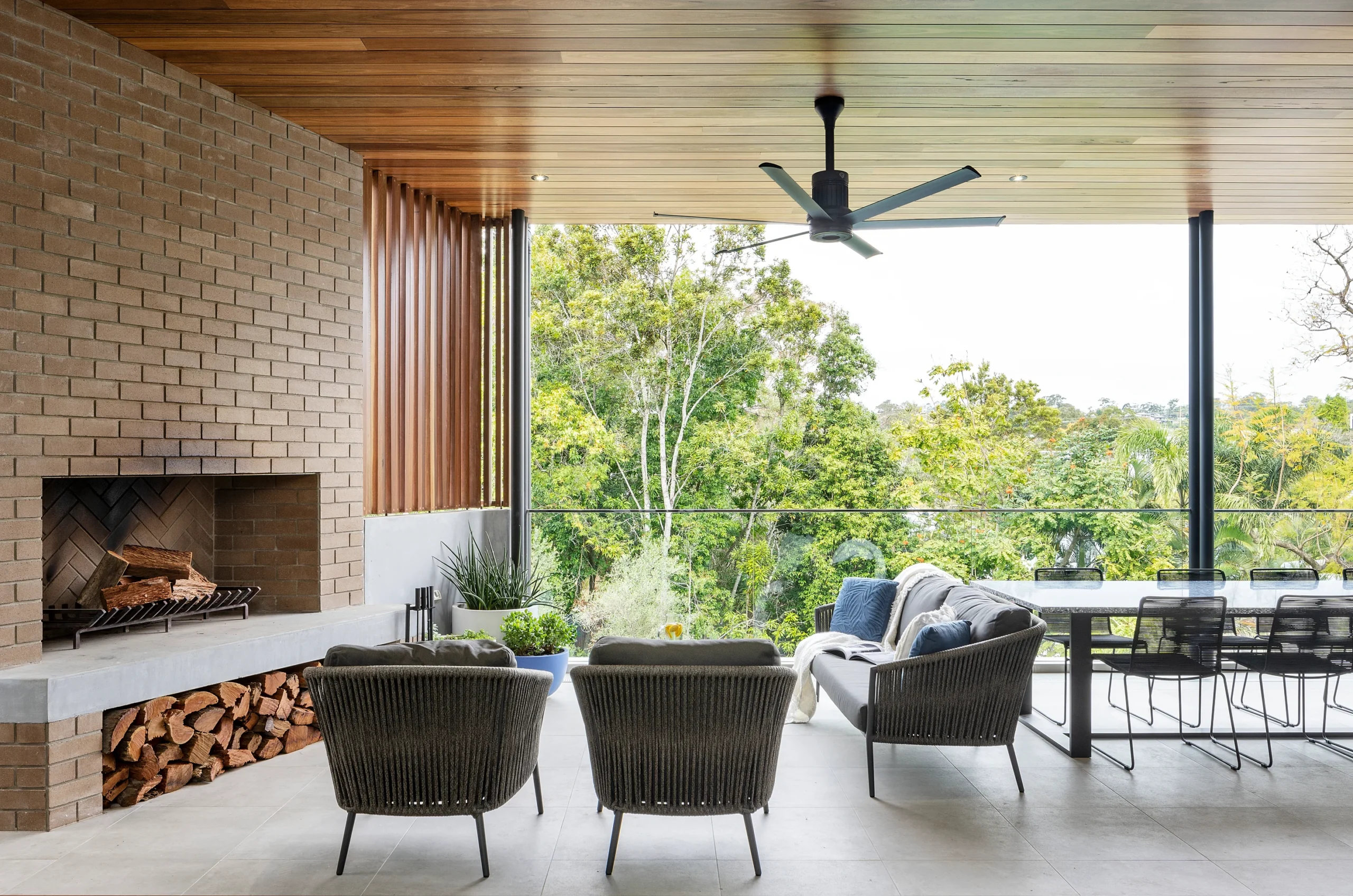 Covered outdoor area with black ceiling fan, brick fireplace, and garden view