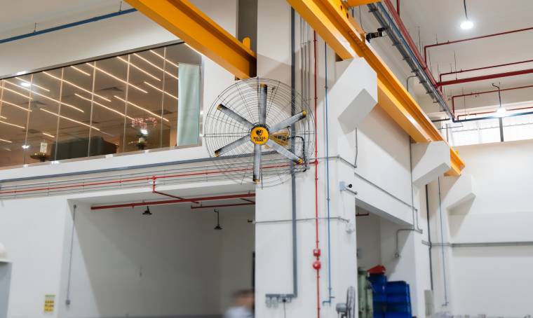 A large industrial building interior featuring a ceiling fan, with a man walking past in the foreground.