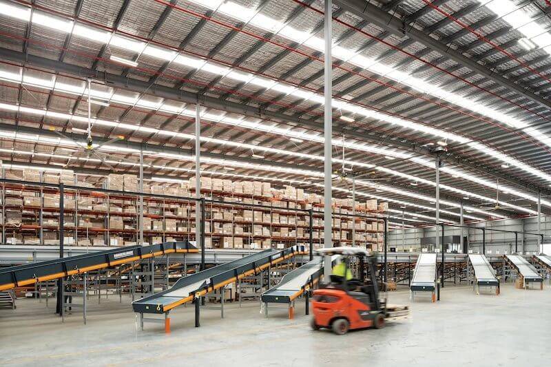 A forklift truck navigating through a spacious warehouse filled with shelves and boxes.