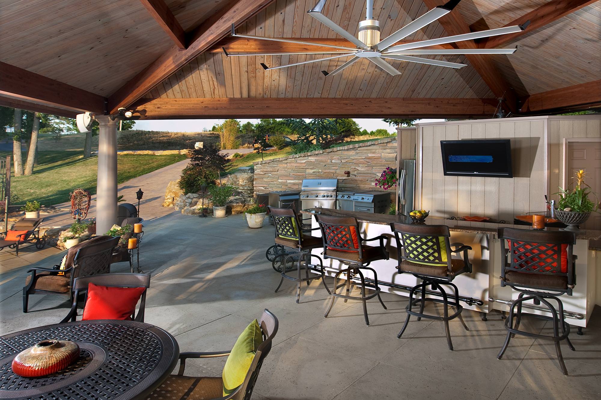 outdoor venue with a large ceiling fan, kitchen, and tables with chairs.