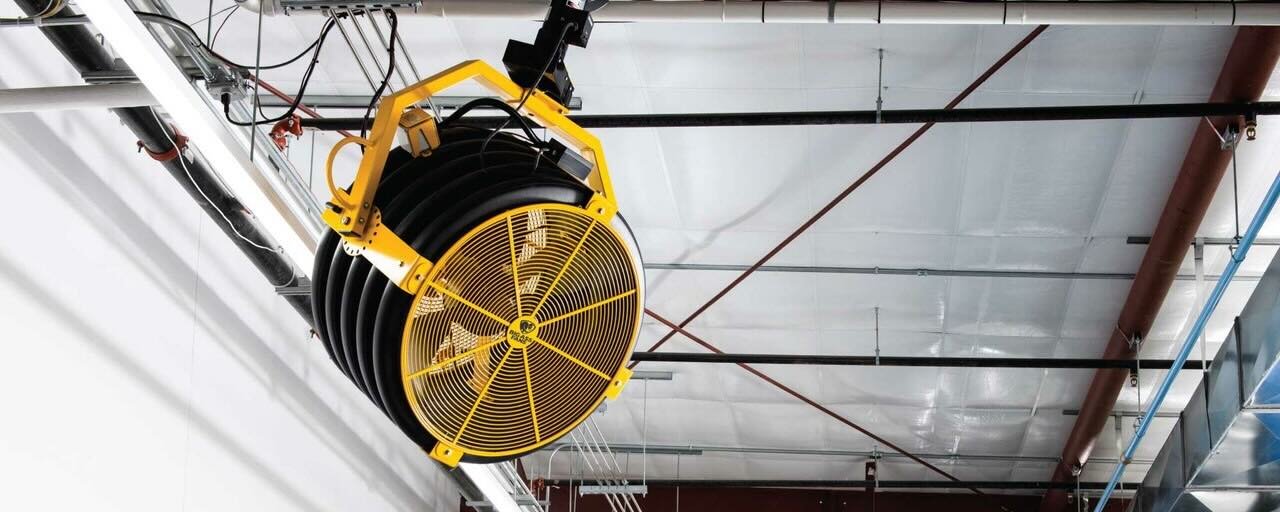 A large industrial oscillating fan by Big Ass Fans is positioned high in a warehouse to provide optimal airflow.