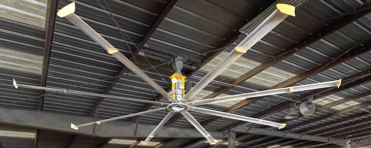 Looking up at the ceiling inside a large warehouse, with an HVLS Ceiling Fan by Big Ass Fans expertly installed.