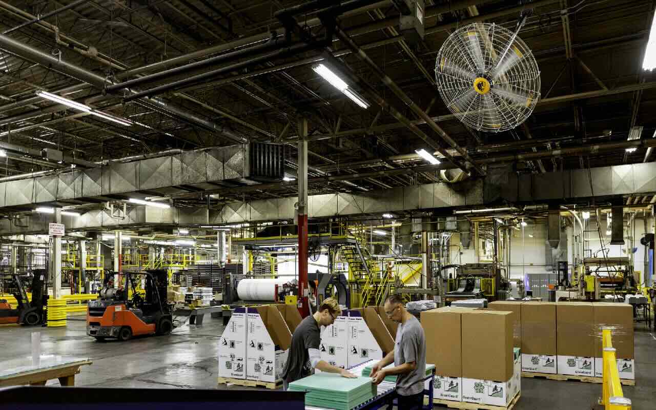 Inside a busy warehouse looking at an assembly line with two people working productively under a high-velocity fan expertly placed by Big Ass Fans.