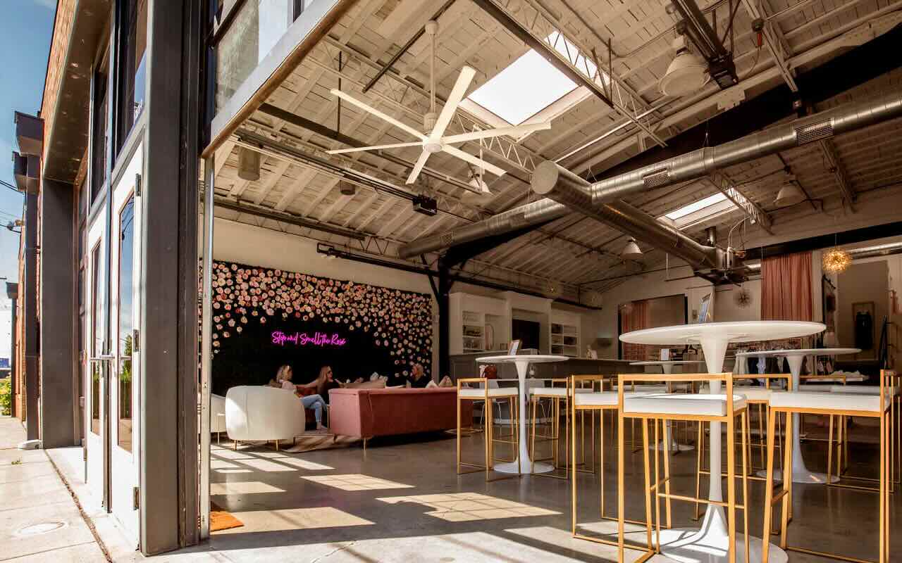 Looking into a business that has an open-air area that leads into a commercial space currently occupied by patrons enjoying time together in a seating area while the room is cooled by the Big Ass Fan installed expertly.