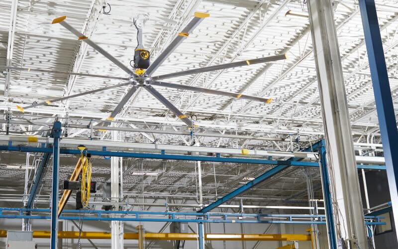 Inside a large warehouse facility, looking toward the ceiling where a large HVLS fan by Big Ass Fans is installed.