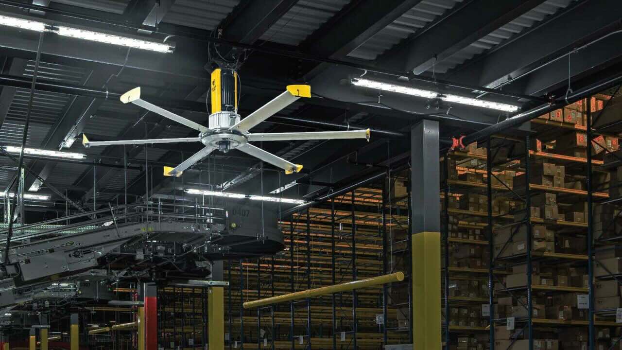 An upward view from inside a large warehouse with ceiling lights and a ceiling fan by Big Ass Fans.