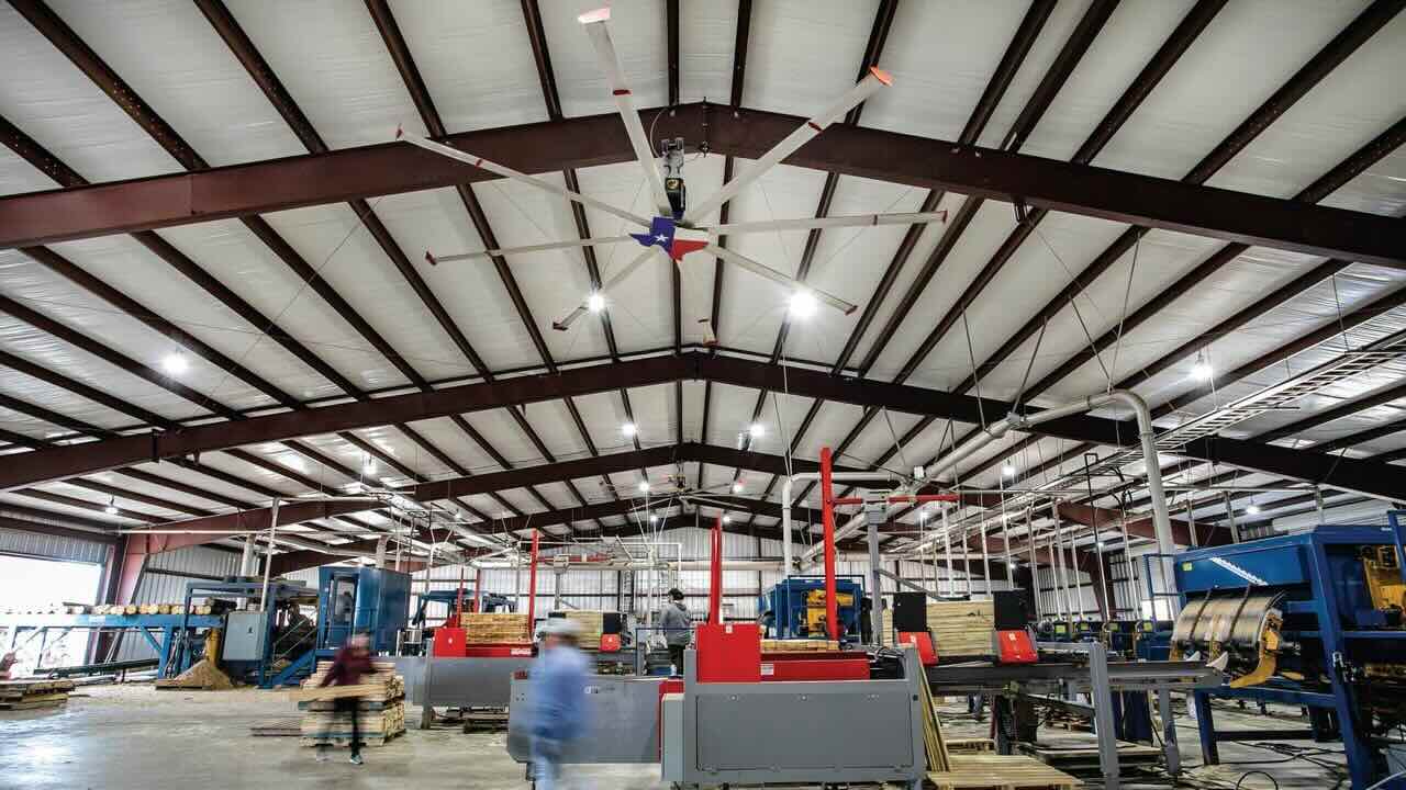 Inside an expansive, modern warehouse facility in Texas, we see a customized HVLS fan by Big Ass Fans professionally installed for optimal airflow for the employees and machines in the warehouse.