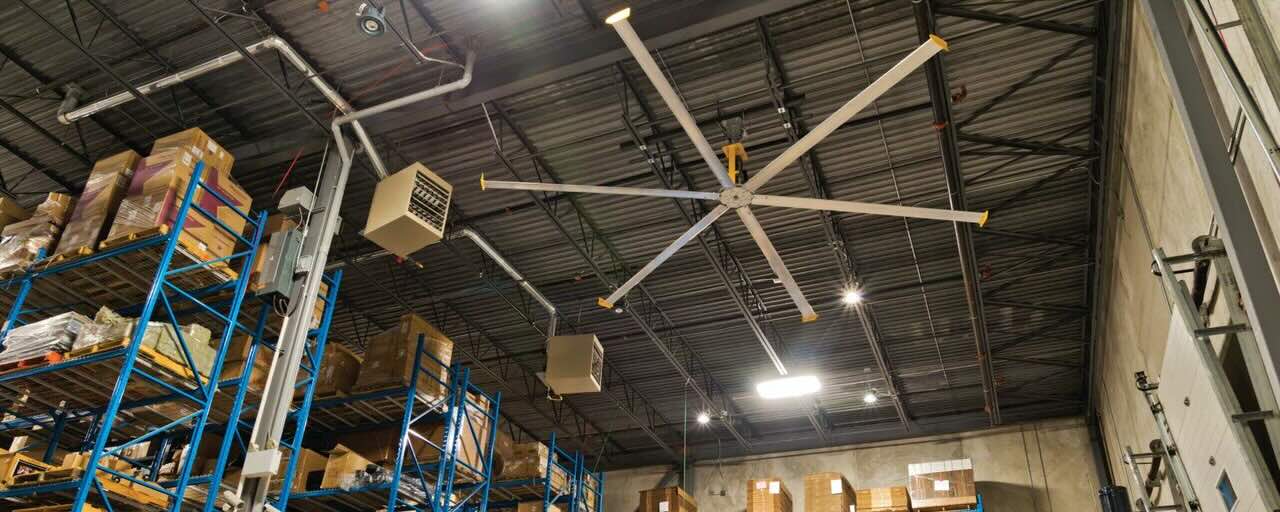 Inside a large and busy warehouse, an hvls ceiling fan by Big Ass Fans is installed for optimal airflow.