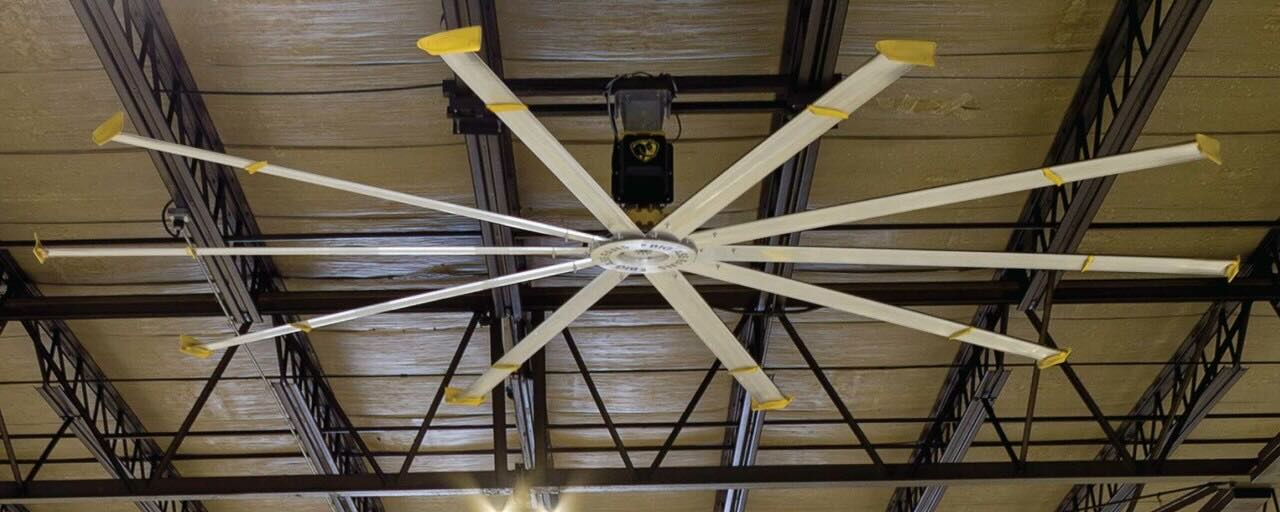 The view of a high ceiling in a warehouse with rafters and an expertly installed HVLS ceiling fan by Big Ass Fans.