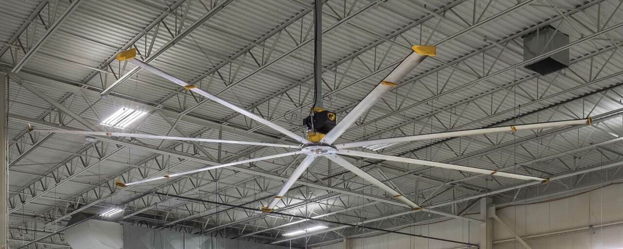 The view from inside a large warehouse, looking up at the ceiling where there is a large HVLS fan by Big Ass Fans installed.