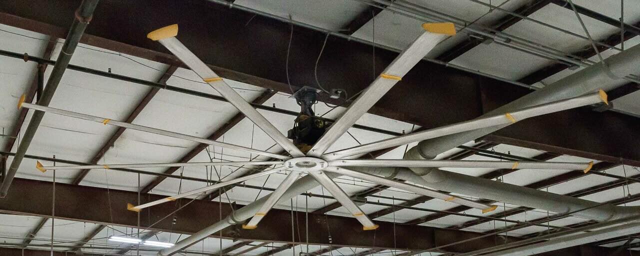 Looking upward at a high warehouse ceiling, with an HVLS Fan by Big Ass Fans expertly installed for optimal airflow.