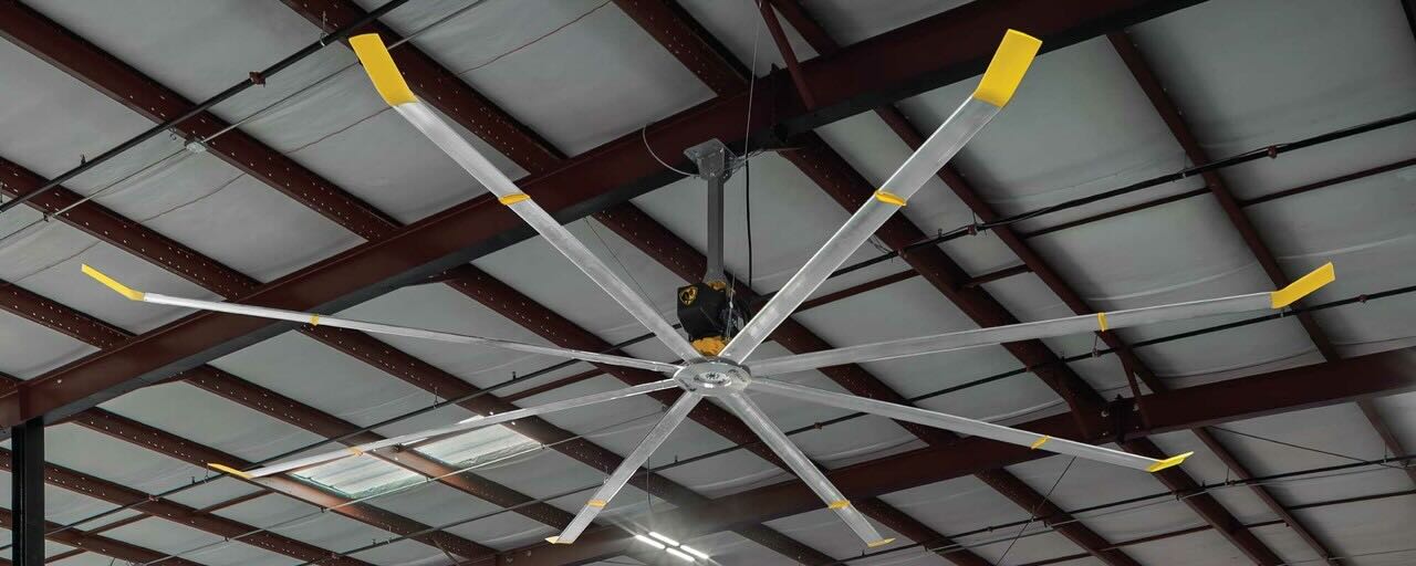 The view of a large warehouse ceiling, with a large HVLS fan by Big Ass Fans installed and providing airflow.