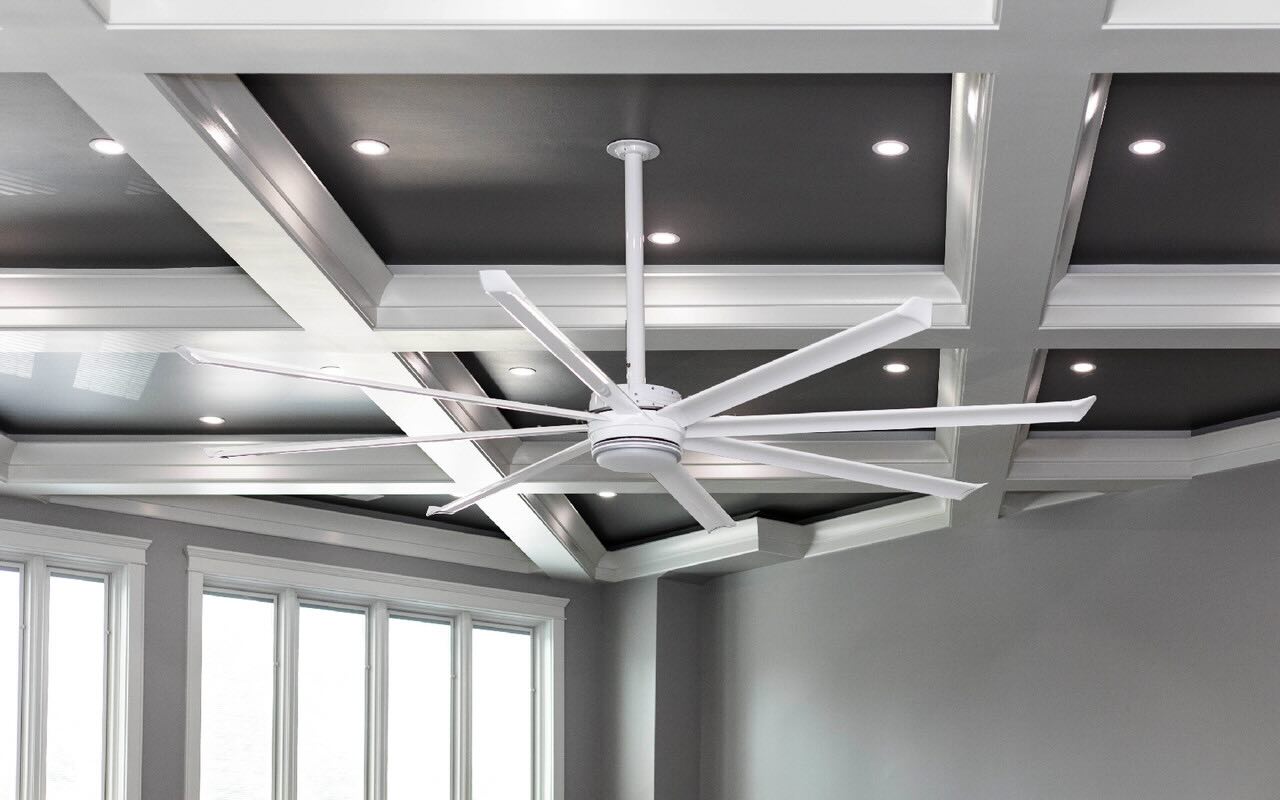 Looking up at the ceiling in a modern room, walls in gray with windows surrounded in white accents and the room cooled by a ceiling fan made and installed by Big Ass Fans.