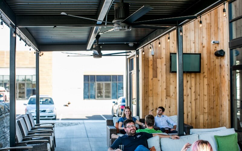 Several customers enjoy an outdoor seating area for a local business, cooled by expertly installed ceiling fans by Big Ass Fans.